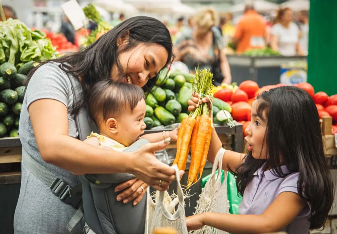 Mother, baby, and child buying carrots at grocery store